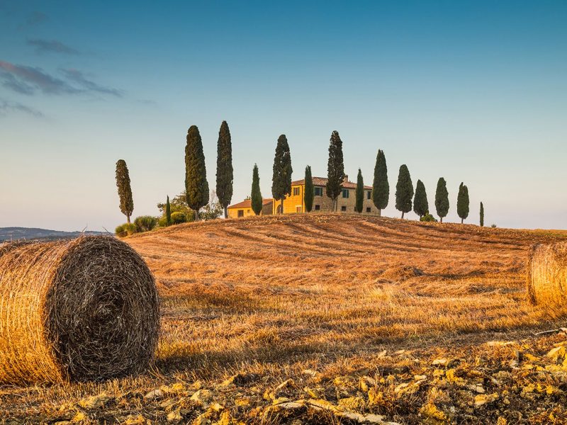 Beautiful Tuscany landscape with traditional farm house and hay bales in golden evening light, Val d'Orcia, Italy
